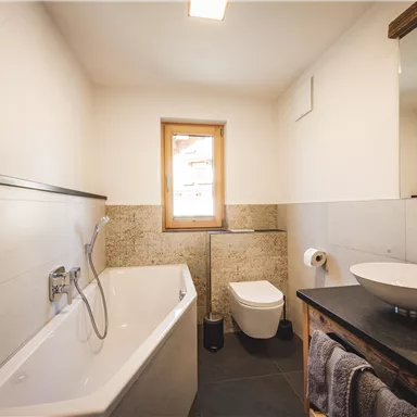 A modern bathroom with a bathtub, sink, and toilet. The light comes through a window and creates a bright, inviting atmosphere.