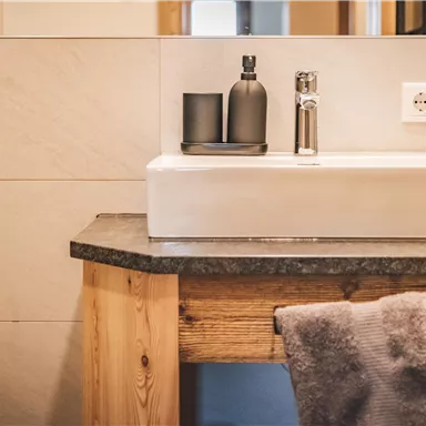 A modern sink on a wooden table in a stylish bathroom. The walls are bright and simply designed, with subtle decorative elements.