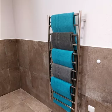 Ein Handtuchhalter mit mehreren gefalteten Handtüchern in Blau und Grau. Die Wand ist hell und die Fliesen sind dunkel.