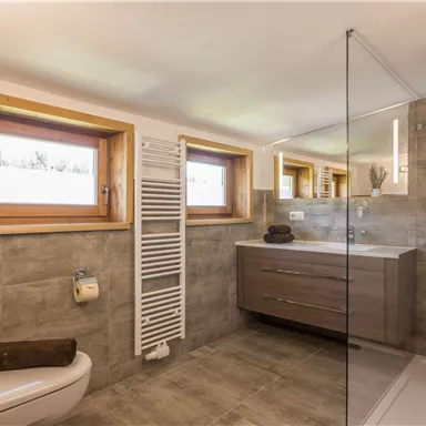 Ein modernes Badezimmer mit einer großen Dusche und einem stilvollen Holzwaschtisch. Die Fenster sorgen für viel Tageslicht und eine angenehme Atmosphäre.