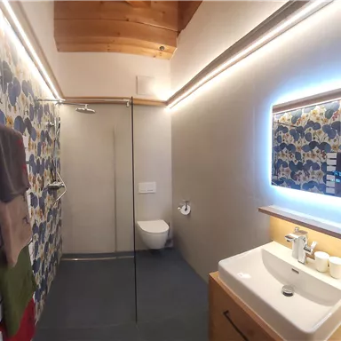 Ein modernes Badezimmer mit einer Dusche und einem eleganten Waschbecken. Die Wände sind mit buntem Muster und Holzverkleidung dekoriert.