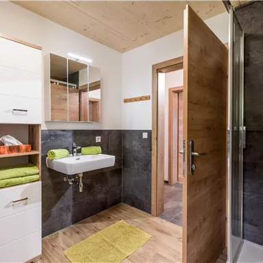 A modern bathroom with a sink, mirror, and shower area. The walls are painted in neutral colors, and there are towels and a bath mat in fresh shades of green.