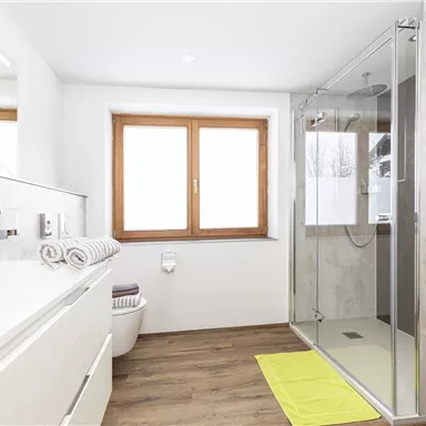 Ein modernes Badezimmer mit einer großen Dusche und einem hellen Fenster. Die Ausstattung ist sauber und gut strukturiert, mit einem eleganten Waschbecken und Handtüchern.