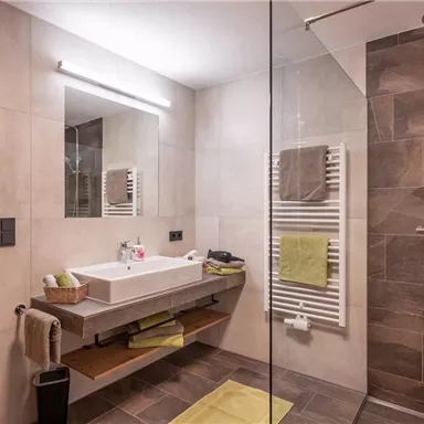 A modern bathroom with a large shower and an elegant sink. The walls are bright and there is great lighting.