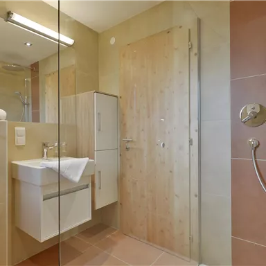 Ein modernes Badezimmer mit Dusche, Waschbecken und hellen Fliesen. Handtücher liegen bereit, und die Einrichtung ist minimalistisch.