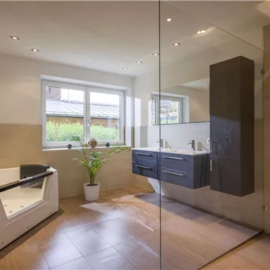 Ein modernes Badezimmer mit einer Badewanne und einer Dusche. Große Fenster lassen viel Licht herein und es gibt eine Pflanze zur Dekoration.