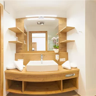 Ein modernes Badezimmer mit Holzdetails und einem großen Waschbecken. Die Wände sind in neutralen Farben gehalten und das Licht sorgt für eine einladende Atmosphäre.