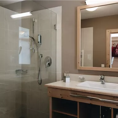 Ein modernes Badezimmer mit einer Dusche und einem großen Spiegel. Die Wände sind in neutralen Farben gehalten und es gibt Holzdetails.