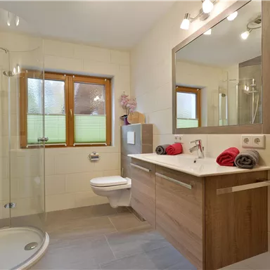 Ein modernes Badezimmer mit einer Duschkabine und einem großen Spiegel. Die Wände sind in neutralen Farbtönen gehalten und es gibt helle Handtücher auf der Ablage.