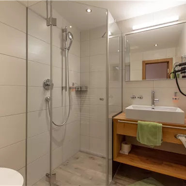 Ein modernes Badezimmer mit einer abgeschlossenen Dusche und einem klaren Spiegel. Die Holzablage bietet Platz für Handtücher und Pflegeprodukte.