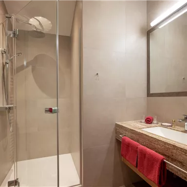 Ein modernes Badezimmer mit einer Glasdusche und einem eleganten Waschbecken. Rote Handtücher und ein Spiegel ergänzen das stilvolle Design.
