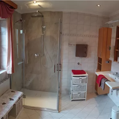 A modern bathroom with a walk-in shower and bright tiles. On the left side, there is a window and a bench.