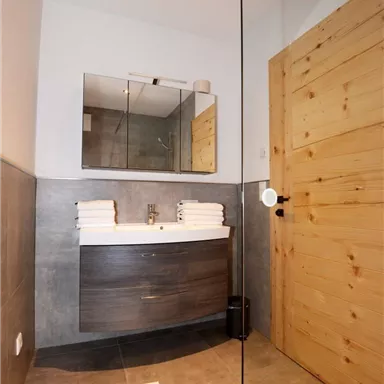 Ein modernes Badezimmer mit einem stilvollen Waschbecken und frischen Handtüchern. Die Wände sind in neutralen Tönen gehalten, und die Holzdetails verleihen Wärme.