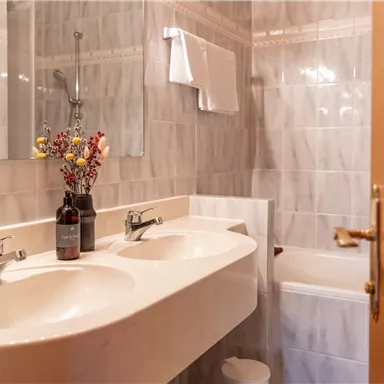 Ein modernes Badezimmer mit einem Doppelwaschbecken und einem Spiegel. Eine hübsche Blumendekoration sorgt für einen einladenden Akzent.