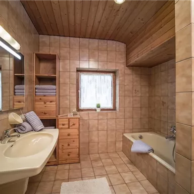 Ein modernes Badezimmer mit Fliesen in warmen Farbtönen. Es enthält eine Badewanne, ein Waschbecken und einen Holzschrank.