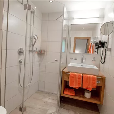 Ein modernes Badezimmer mit einer Dusche, Waschbecken und handtuch. Orangefarbene Handtücher sorgen für einen frischen Akzent.