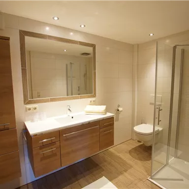 Ein modernes Badezimmer mit Holzschränken und einem großen Spiegel. Es gibt eine Dusche und eine helle, freundliche Atmosphäre.