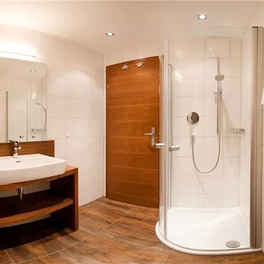 Ein modernes Badezimmer mit Dusche, Waschbecken und Holzregalen. Helle Fliesen und angenehme Beleuchtung schaffen eine einladende Atmosphäre.