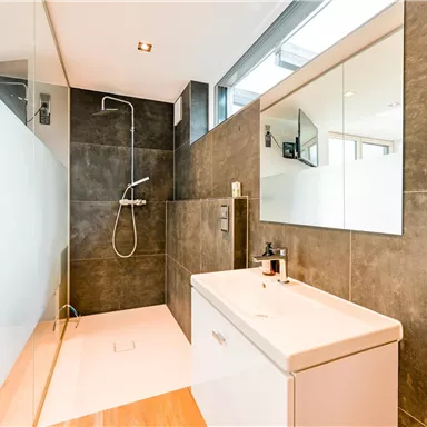 Ein modernes Badezimmer mit eleganten, grauen Wänden und einer großen Dusche. Der Waschbeckenbereich ist hell und funktional gestaltet.