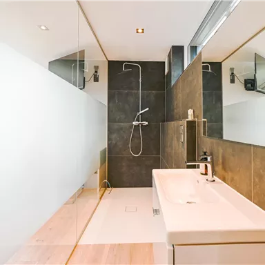 Ein modernes Badezimmer mit einer großen, begehbaren Dusche und eleganten Spiegeln. Die Wände sind in neutralen Tönen gehalten, was einen stilvollen und geräumigen Eindruck vermittelt.