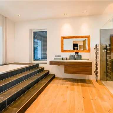 Ein modernes Badezimmer mit einer freistehenden Badewanne und einer großen Duschkabine. Die Holz- und Steinoberflächen sorgen für ein elegantes Ambiente.