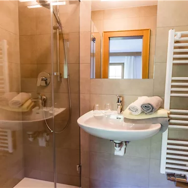 Ein modernes Badezimmer mit einer Dusche, einem Waschbecken und Handtüchern. Die Wände sind mit hellen Fliesen gefliest und es gibt einen Handtuchtrockner.