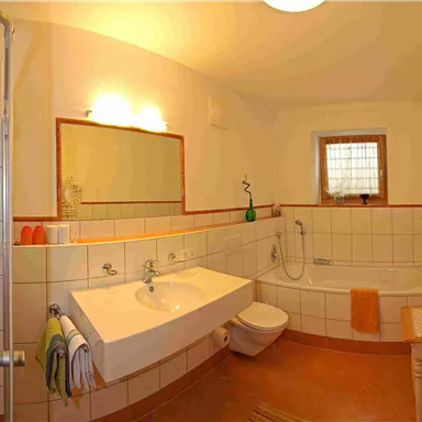 Ein modernes Badezimmer mit einer Dusche, einer Badewanne und einem Waschbecken. Es gibt orangefarbene Handtücher und eine helle, freundliche Beleuchtung.