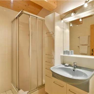 Ein modernes Badezimmer mit einer Dusche und einem Waschbecken. Die Wände sind hell und die Ausstattung ist schlicht und funktional.