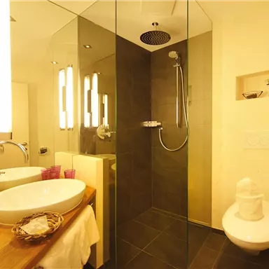 Ein modernes Badezimmer mit einer gläsernen Dusche und einer eleganten Badewanne. Die dekorativen Details und die sanfte Beleuchtung schaffen eine entspannende Atmosphäre.