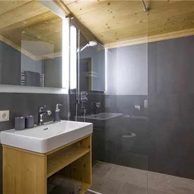 Ein modernes Badezimmer mit einer Holzdecke und dunklen Wänden. Es verfügt über ein Waschbecken mit Holzunterbau und große Spiegel.