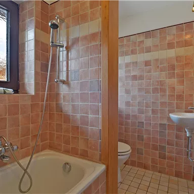 A bathroom with a bathtub and a shower. The walls are tiled with light, tile-like tiles.