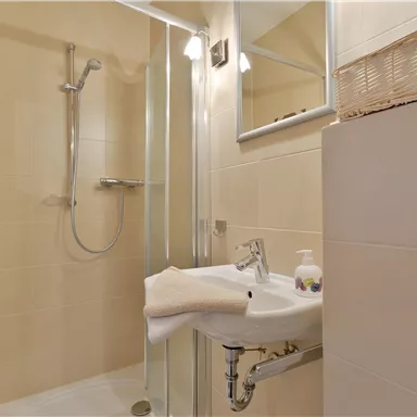 Ein modernes Badezimmer mit einer Duschkabine und einem Waschbecken. Die Wände sind in einem hellen Beige gehalten, was einen sauberen Eindruck vermittelt.