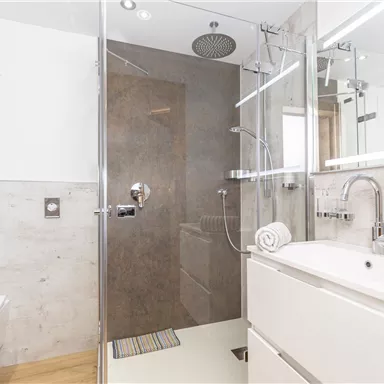 Ein modernes Badezimmer mit gläserner Dusche und eleganten Armaturen. Helle Wände und ein Holzfußboden schaffen eine einladende Atmosphäre.