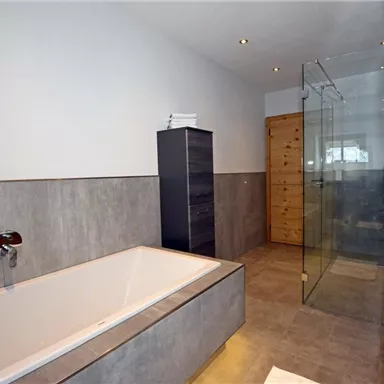 Ein modernes Badezimmer mit einer Badewanne und einer Glasdusche. Die Wände sind in einem neutralen Farbton gehalten und die Einrichtung ist schlicht und stilvoll.