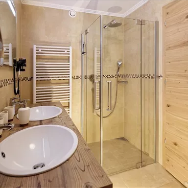 A modern bathroom with two sinks and a large glass shower. The walls are in warm tones, complemented by wooden details.