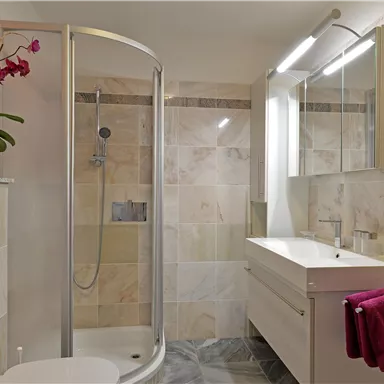 Ein modernes Badezimmer mit einer Dusche und einem eleganten Waschtisch. Dekorative Blumen und ein Handtuch verleihen dem Raum einen stilvollen Touch.