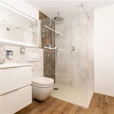 Ein modernes Badezimmer mit einer Glaskabine für die Dusche und einem eleganten Waschbecken. Helle Wände und ein Holzfußboden sorgen für eine freundliche Atmosphäre.