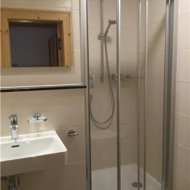 Ein modernes Badezimmer mit einer Dusche und einem Waschbecken. Die Wände sind hell gefliest und es gibt ein Fenster.