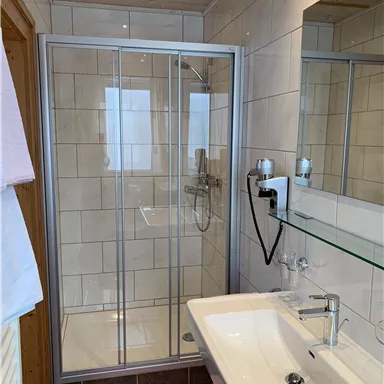 Ein modernes Badezimmer mit einer Duschkabine und einem Waschbecken. Die Wände sind mit fliesen verziert und es gibt eine große Spiegeloberfläche.