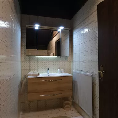 Ein modernes Badezimmer mit einer Holzwaschbeckenunterschränke und Spiegel. Die Wände sind mit hellen Fliesen gefliest und es gibt gute Beleuchtung.