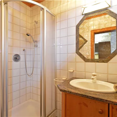 A modern bathroom with a shower cabin and a round mirror. Towels and a soap dish are on the shelf.