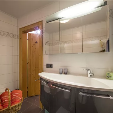A modern bathroom with a rounded sink and a large mirror. On the left side, there is a basket with towels.
