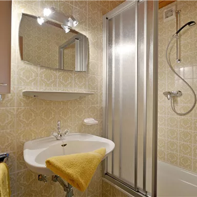 Ein kleines Badezimmer mit einer Dusche und einem Waschbecken. An der Wand hängen Handtücher in pink und gelb.