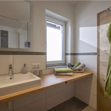A modern bathroom with a wooden sink and a large mirror. Towels in various shades of green are placed on the shelf.