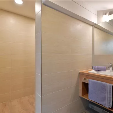 Ein modernes Badezimmer mit hellen Fliesen und einem stilvollen Waschbecken. Handtücher in sanften Farben liegen ordentlich bereit.