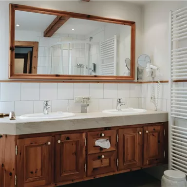 Ein modernes Badezimmer mit zwei Waschbecken und Holzschränken. Es gibt einen großen Spiegel und helle Fliesenwände.