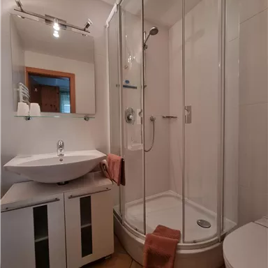 Ein modernes Badezimmer mit einer gläsernen Duschkabine und einem Waschbecken. Die Wände sind hell und der Boden ist gefliest.