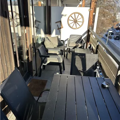 Ein gemütlicher Balkon mit schwarzen Möbeln und einem Steuerrad an der Wand. Der Platz bietet einen Blick auf die Umgebung und lädt zum Entspannen ein.