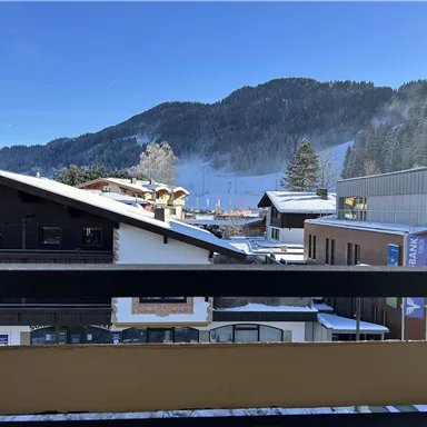 Eine winterliche Landschaft mit schneebedeckten Dächern und Bergen im Hintergrund. Der klare blaue Himmel sorgt für eine frische Atmosphäre.