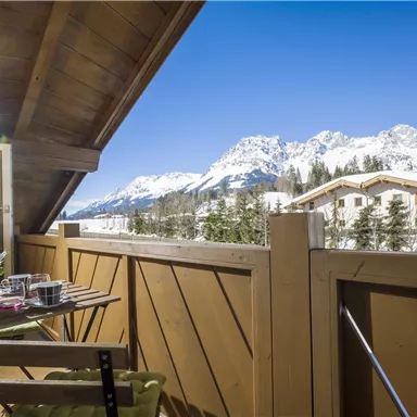 Ein gemütlicher Balkon mit Blick auf schneebedeckte Berge. Der Himmel ist klar und blau, und es gibt eine kleine Pflanze auf dem Tisch.